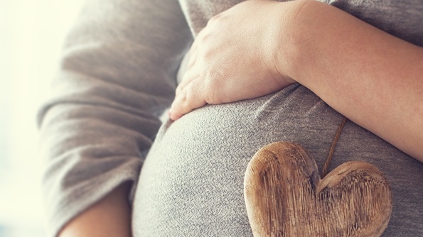 young pregnant woman holds wooden heart. love concept. pastel to