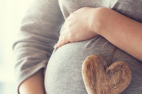 young pregnant woman holds wooden heart. love concept. pastel to