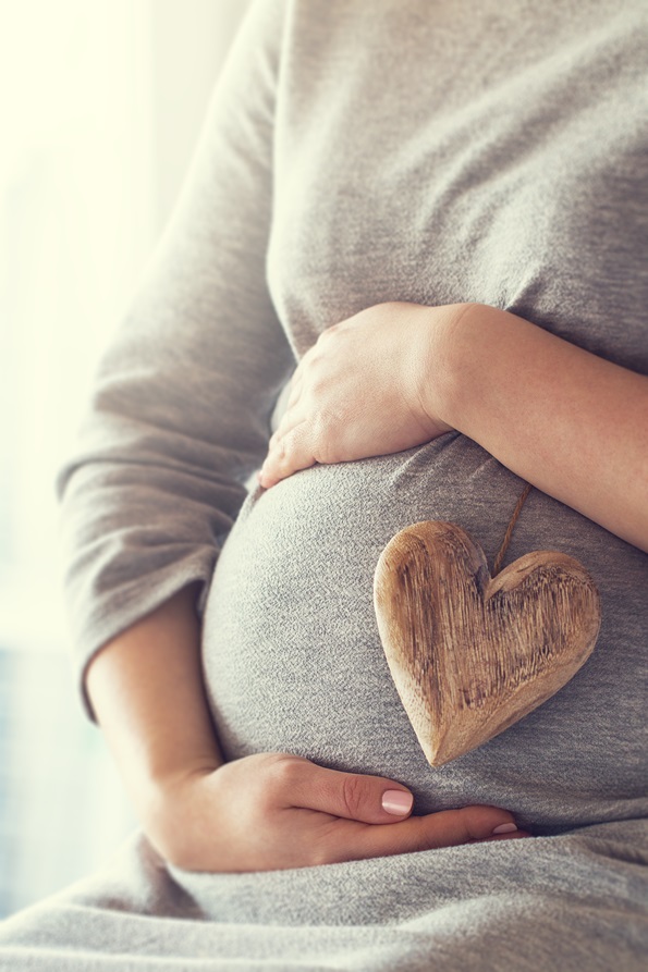 young pregnant woman holds wooden heart. love concept. pastel to